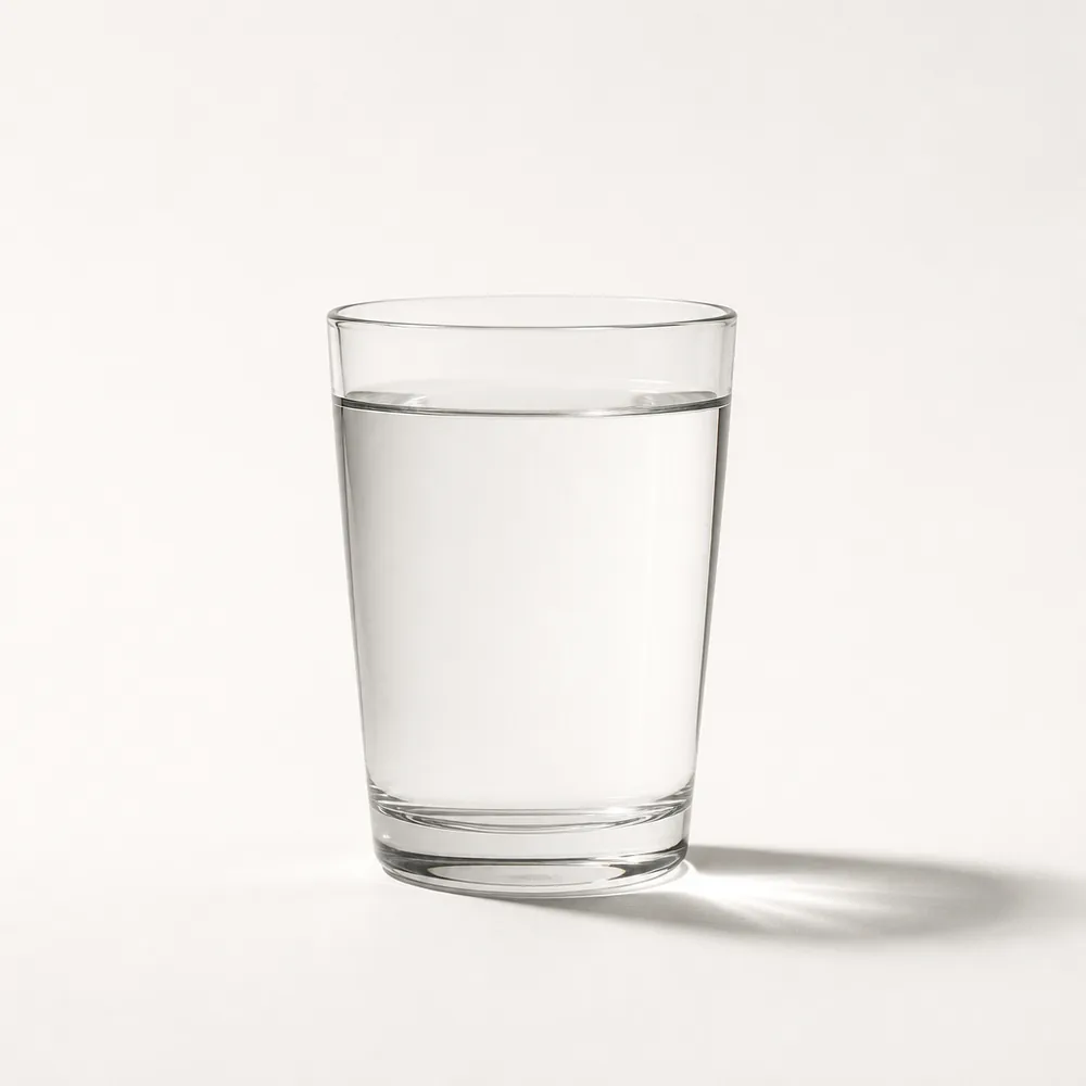 A single glass of clear oral rehydration solution lit like a museum artifact against a pale background.
